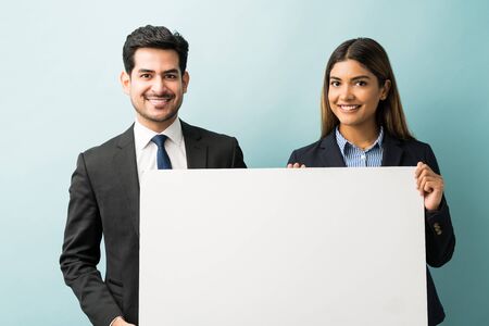 Portrait of smiling business executives holding blank placard while standing against blue backgroundの写真素材