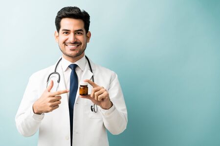 Smiling handsome doctor showing medicine bottle against blue backgroundの写真素材