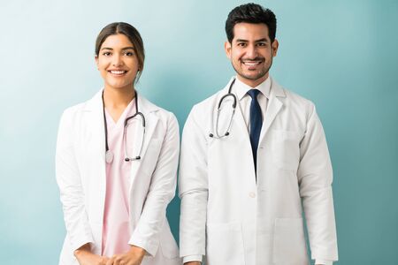 Male and female doctors wearing lab coat standing against colored backgroundの写真素材