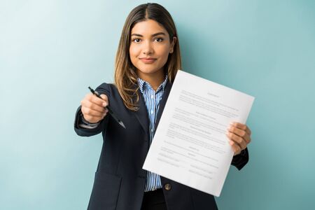 Confident young female professional with contract and pen against colored background
