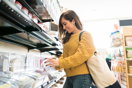 Smiling Caucasian woman carrying bag while shopping food in bulk in supermarket