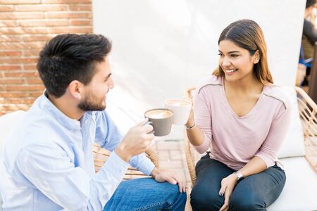 Latin boyfriend and girlfriend toasting coffee cups at cafe during date