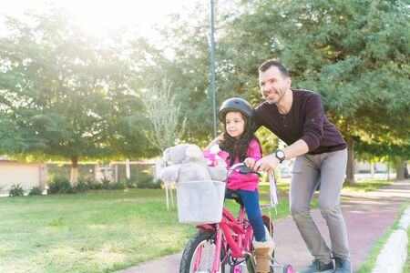 Mid Adult Father Teaching Daughter To Ride Bicycle At Parkの写真素材