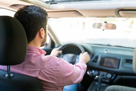 Rear view of Hispanic mid adult man driving new car
