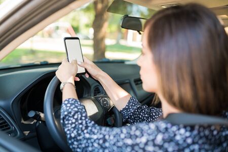 Closeup of woman messaging on smartphone while sitting in car on driver's seat