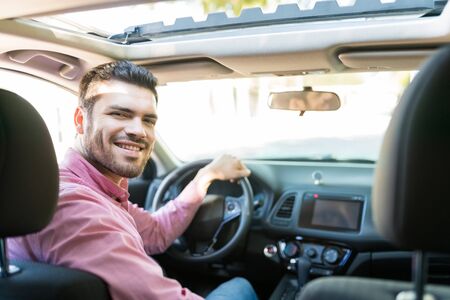Confident Hispanic mid adult man smiling while driving new carの写真素材