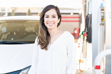 Smiling woman in casual standing by car at gas stationの写真素材