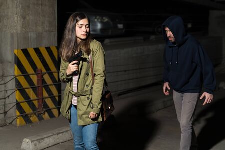 Young Latin woman with gun prepared to fightback against bandit following her in dark alleyの写真素材