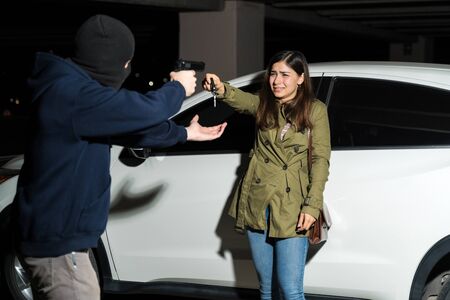 Robber with gun threatening young female victim to give her car keys in parking lot