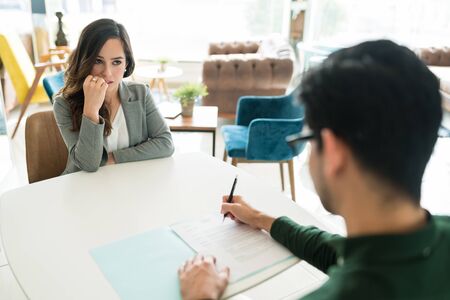 Worried candidate looking at recruiter reading resume in office during interviewの写真素材