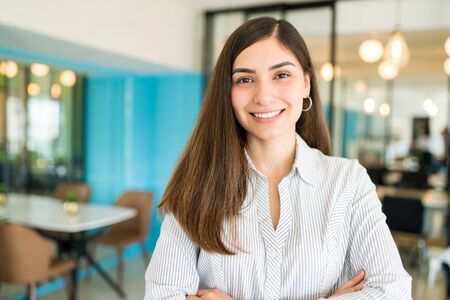 Beautiful smiling businesswoman standing with arms crossed at workplaceの写真素材
