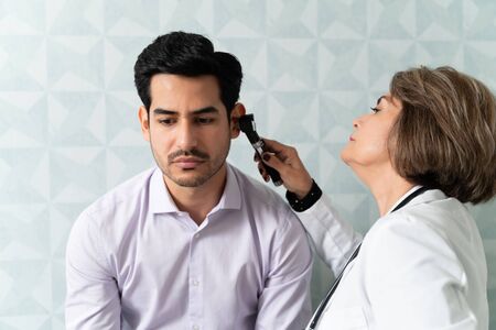 Caucasian female doctor examining patient's ear with otoscope in hospitalの写真素材