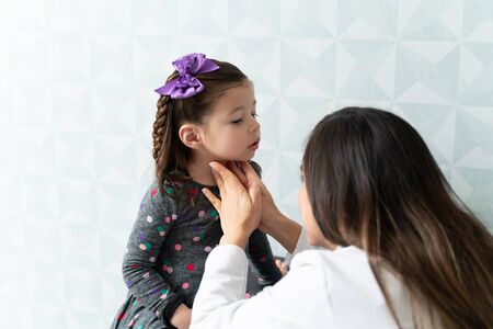 Female pediatrician examining thyroid gland of little girl during medical checkupの写真素材