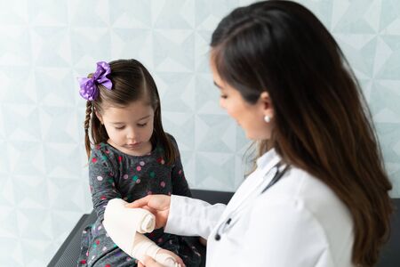 Female doctor putting bandage on little Caucasian girl's hand in clinicの写真素材