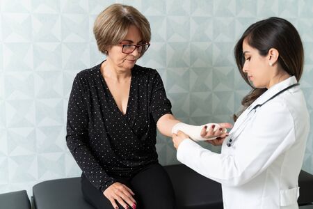 Confident female doctor putting bandage on elderly woman's handの写真素材