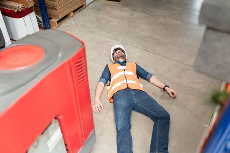 High angle view of male Latin employee lying unconscious on floor at warehouse