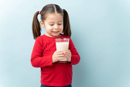 Pretty little girl enjoying a glass of milk and smiling in a studioの写真素材