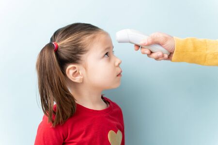 Profile view of an adult hand using a thermometer to check a little girl's temperature in a studioの写真素材