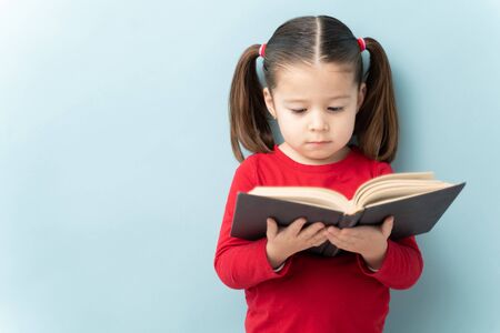 Beautiful Caucasian little girl reading a book in a studio with some copy spaceの写真素材
