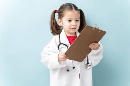 Cute little girl wearing a lab coat and stethoscope and aspiring to be a doctorの写真素材