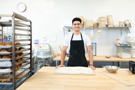 Good looking Hispanic man wearing apron and working in a bakery with a smile