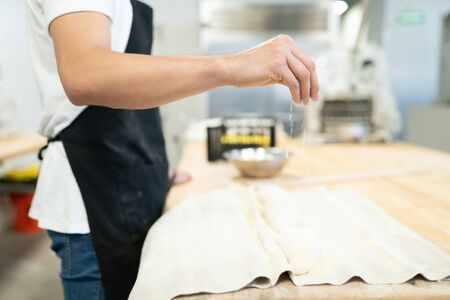 Closeup of a male baker pouring some flour on bread dough and getting some loaves ready for baking