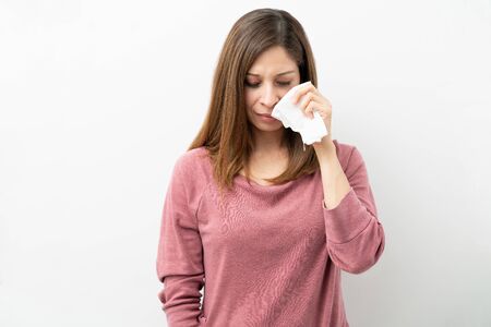 Brunette woman holding a tissue near her face and looking sad and crying in a studio
