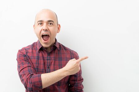 Man in his 30s looking excited and pointing towards copy space with his mouth open in a studioの写真素材