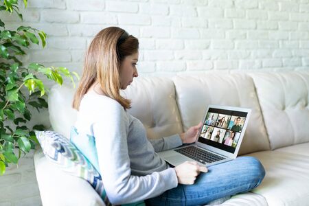 Caucasian woman sitting at home during quarantine and doing a video call for work with some of her...