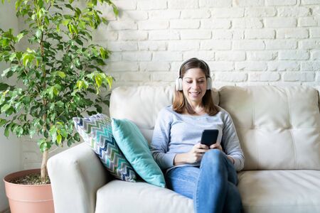 Portrait of a beautiful woman in her 40s wearing headphones and listening to her favorite music at homeの写真素材