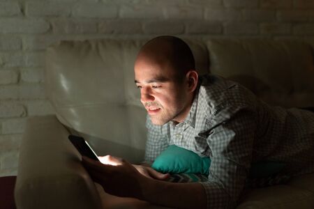 Portrait of a good looking man lying on a couch at home and watching some videos on his smartphone...