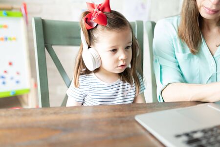 Portrait of an adorable little girl watching videos on a laptop with her mom while wearing...