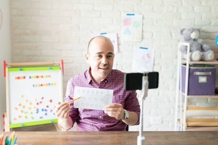Male teacher talking and giving instructions to his students during an online lesson using a...