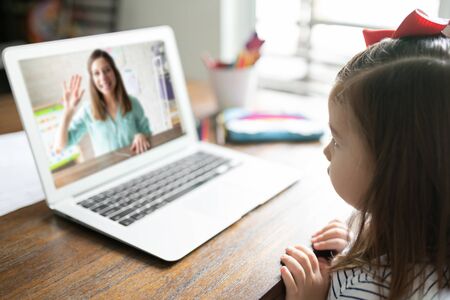 Cute toddler looking at her teacher talk on a computer screen during an online class at home