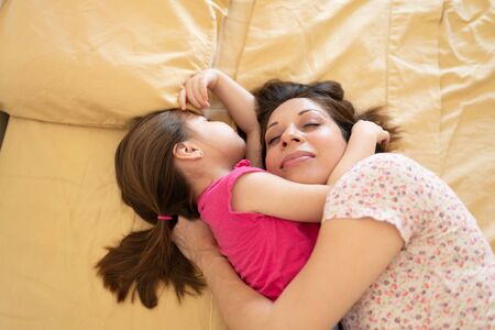 Mother and daughter hugging each other while sharing a bed and cosleeping at homeの写真素材