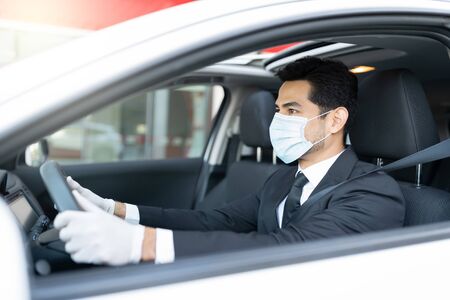 Young male driver wearing gloves and mask while driving car in coronavirus outbreakの写真素材