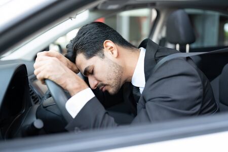 Tired young businessman sleeping on steering wheel in carの写真素材