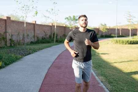 Handsome Hispanic young man jogging on footpath in park