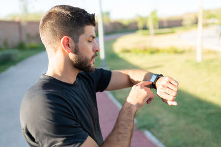 Athletic Latin young man checking time on smartwatch while working out in park