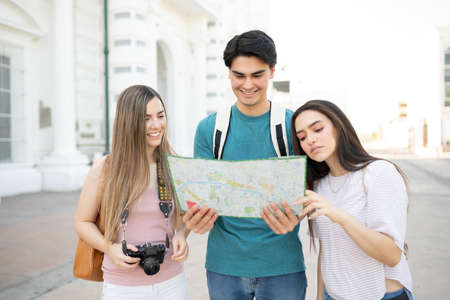 Smiling young tourists looking at map and looking for directions while standing on street in city
