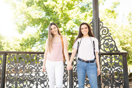 Happy young women holding hands while standing at a park outdoorsの写真素材