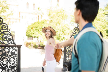 Cheerful young woman holding hand of boyfriend while exploring the city together on a tripの写真素材