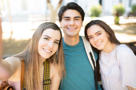 Happy young woman taking selfie with friends at park during trip