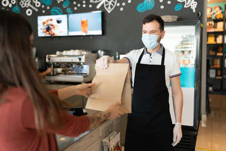 Male staff giving parcel to woman at counter during coronavirus outbreakの写真素材