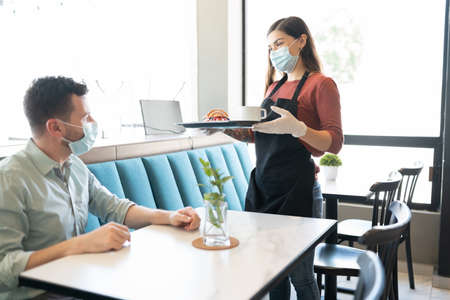 Man looking at waitress serving during coronavirus outbreak in restaurant