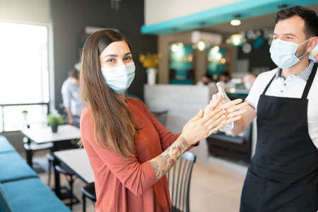 Portrait of customer applying sanitizer on hands given by worker in restaurant