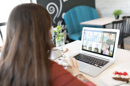 Young woman video calling through laptop in restaurant during coronavirus outbreakの写真素材