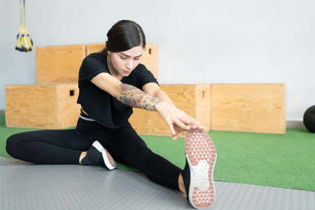 Hispanic young woman touching toe while stretching at health clubの写真素材