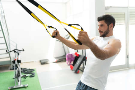 Good looking Latin young man exercising with suspension bands at fitness clubの写真素材