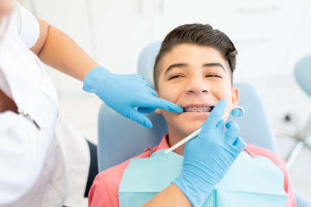 Female dentist examining teenage boy wearing braces